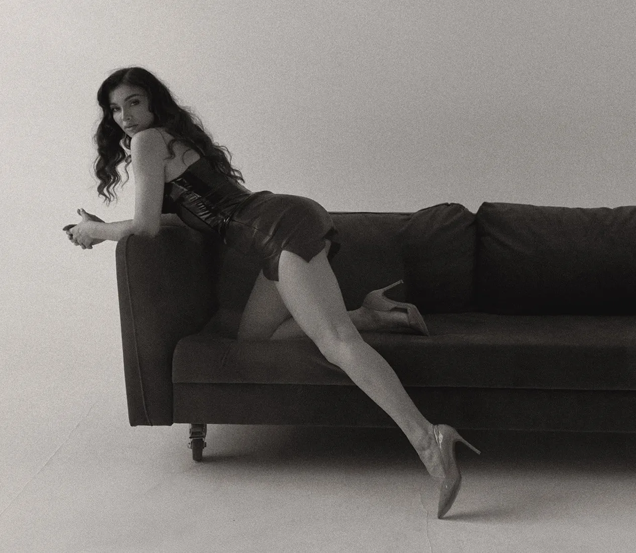Tamara in heels, leaning across a dark sofa, in black and white